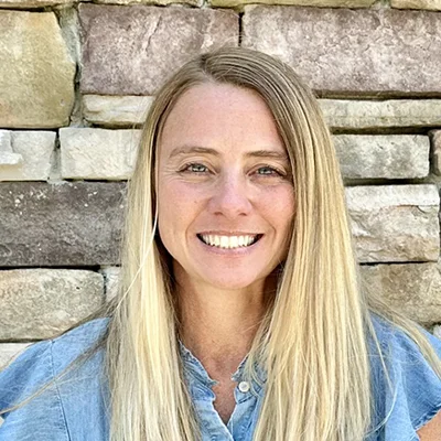 Christi smiling in front of a brick wall.